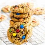 A stack of monster cookies with chocolate chips and M&m's on a cooling rack.