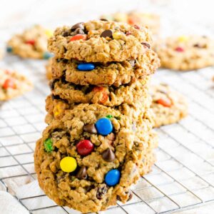 A stack of monster cookies with chocolate chips and M&m's on a cooling rack.