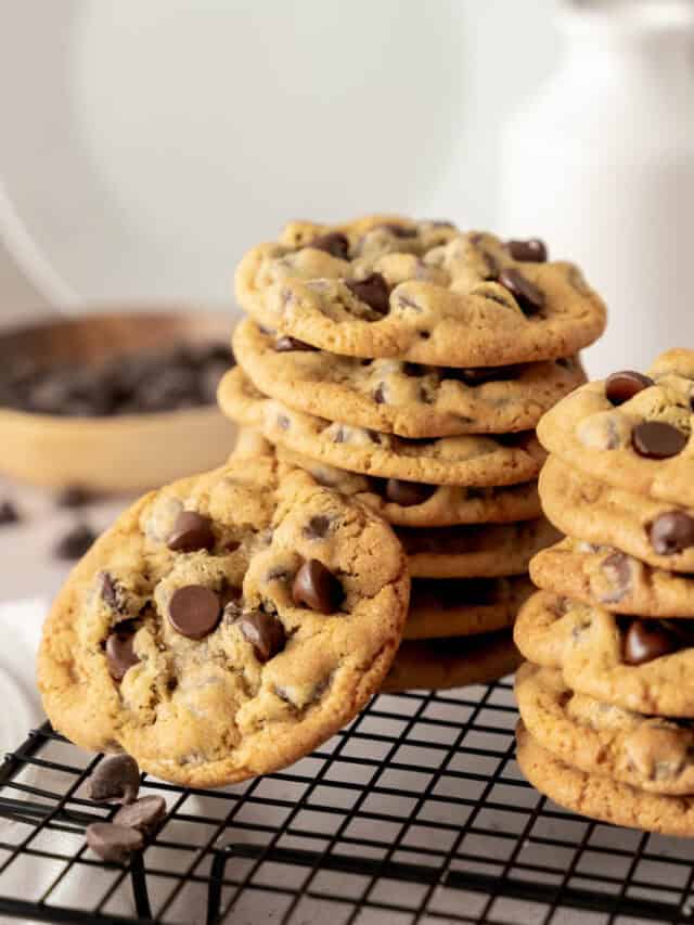 Stacks of chocolate chip cookies with a jar of milk in the background.