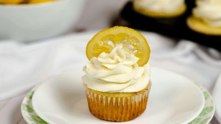 A plate with a lemon vanilla cupcake topped with frosting and garnished with a candied lemon.