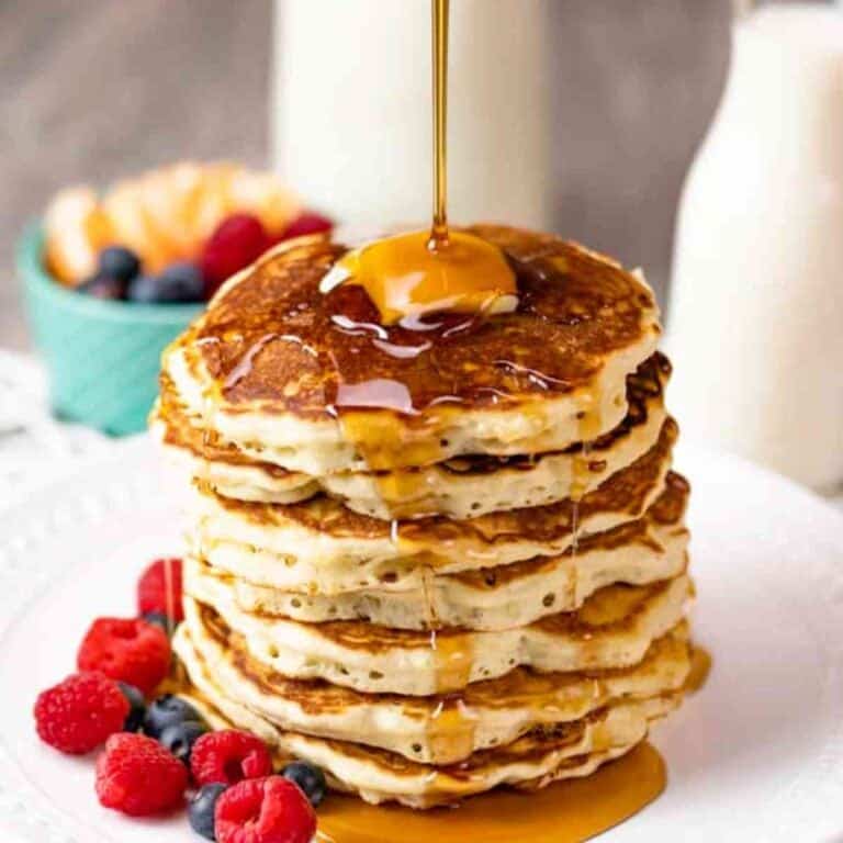 A large stack of brown butter pancakes with syrup poured over the top of a pat of butter.