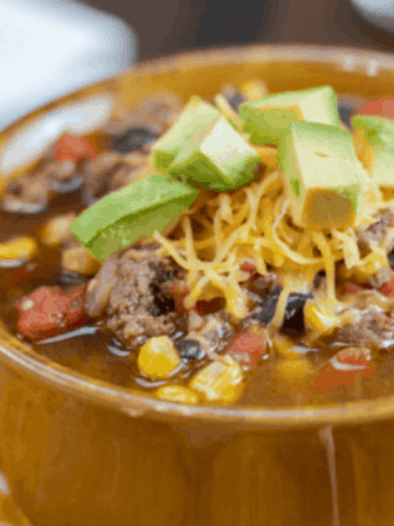 instant pot taco soup in brown bowl with handles. Tortilla chips, and topped with shredded cheese and fresh avocado.
