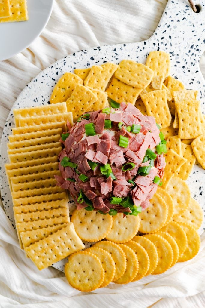 Cheese ball covered in chipped beef and scallions surrounded by a variety of crackers.