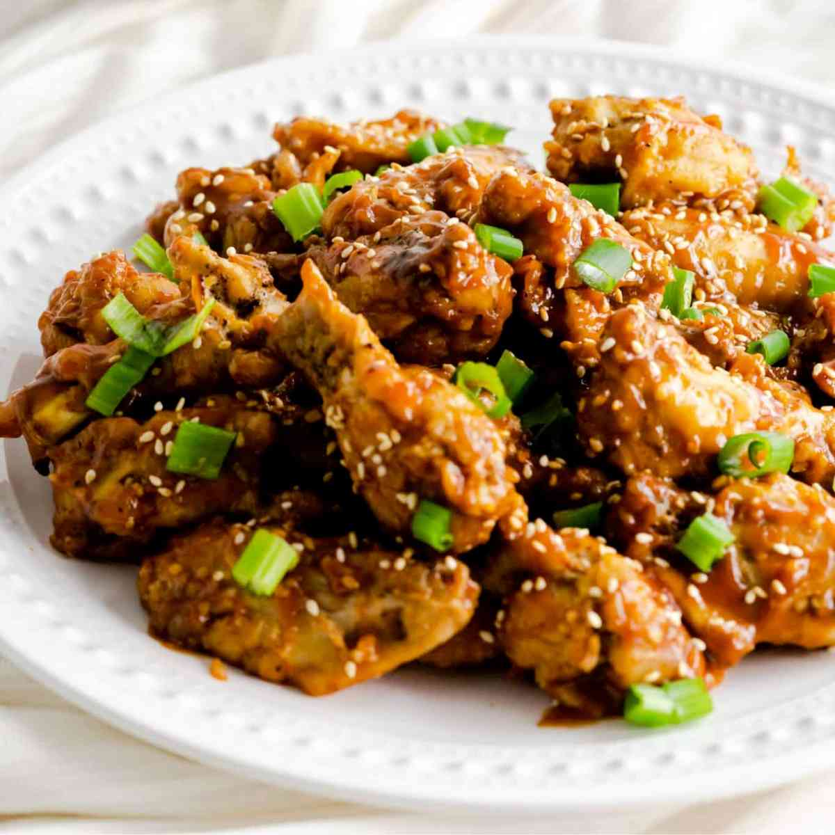 A plate of sweet and salty chicken wings made in the Instant Pot topped with scallions and sesame seeds.