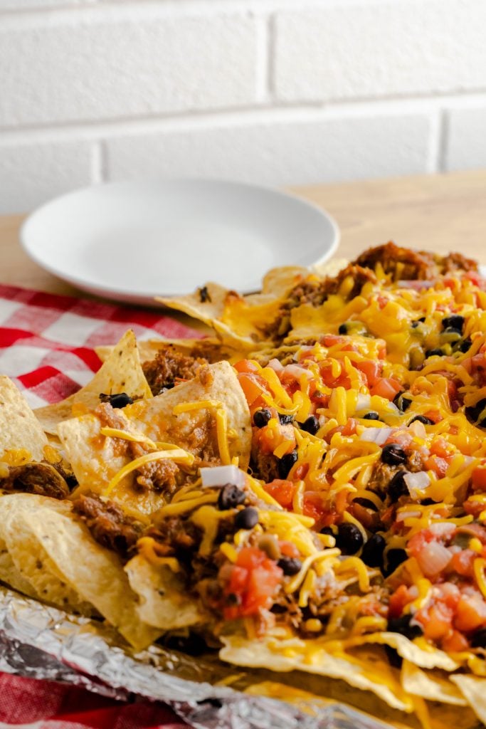 Sheet pan with pulled pork nachos that are tolled with salsa, black beans, and cheese.