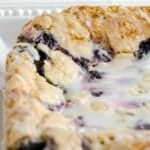 Glazed blueberry lemon bars uncut and on a white plate.