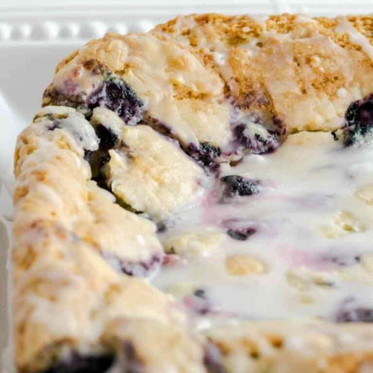 Glazed blueberry lemon bars uncut and on a white plate.