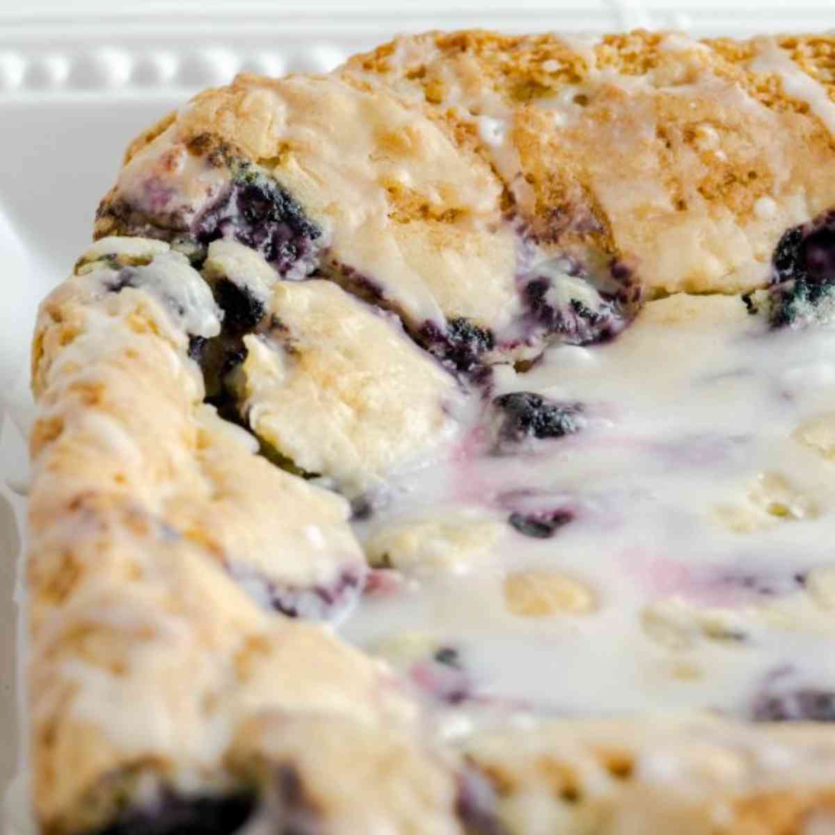 Glazed blueberry lemon bars uncut and on a white plate.