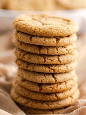 10 chewy gingersnap cookies stacked in center and sitting on brown fabric.