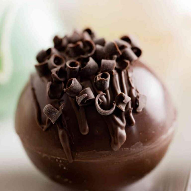 A chocolate hot cocoa bomb topped with chocolate drizzle and chocolate curls.
