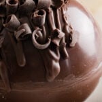 Close up of hot cocoa bowl drizzled with chocolate and garnished with chocolate curls.