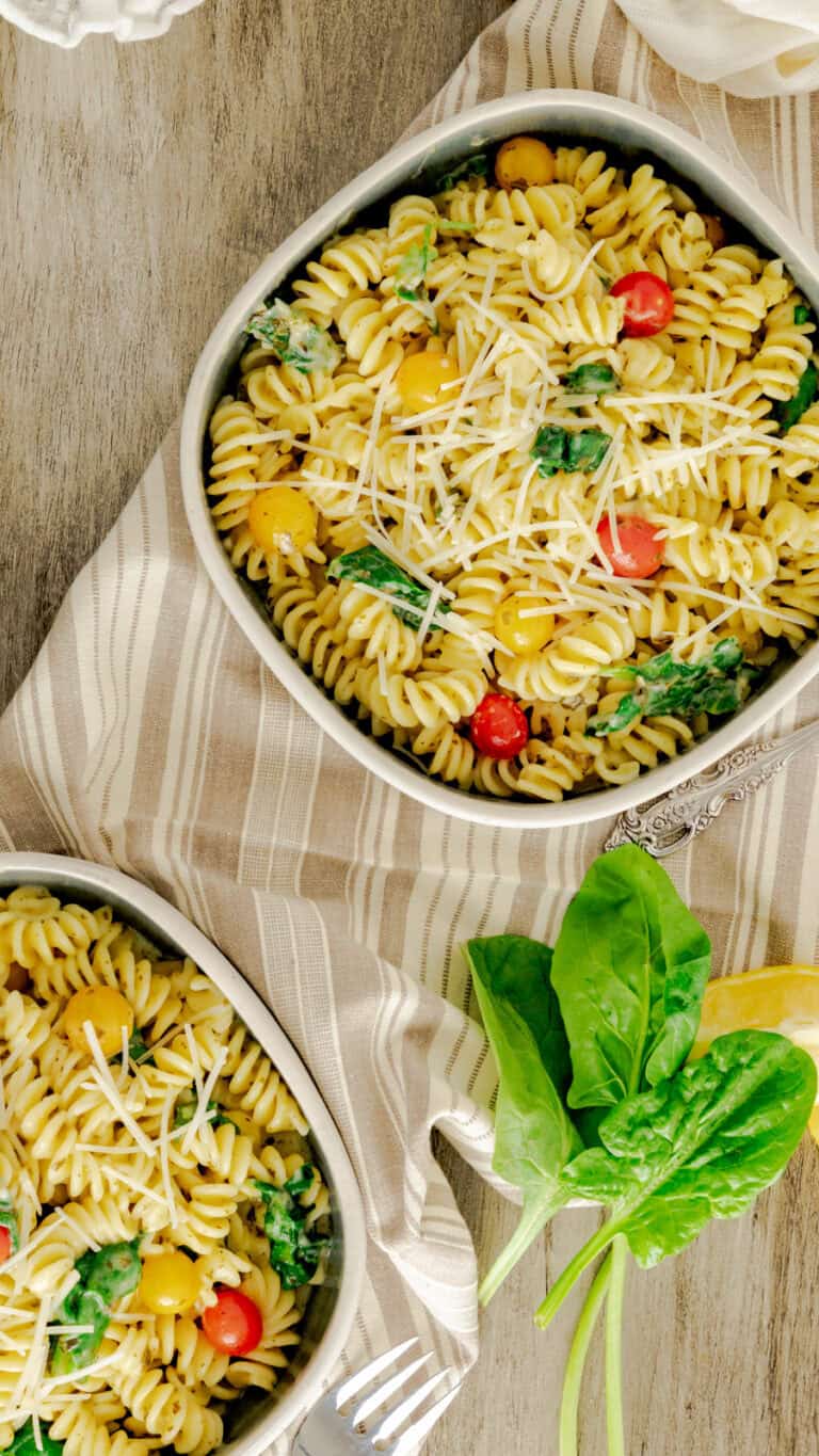 two bowls of pesto pasta topped with Parmesan and cherry tomatoes