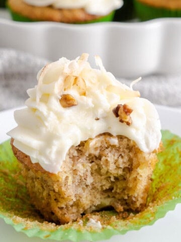 A hummingbird cake cupcake with a bite taken out of it on a white plate.