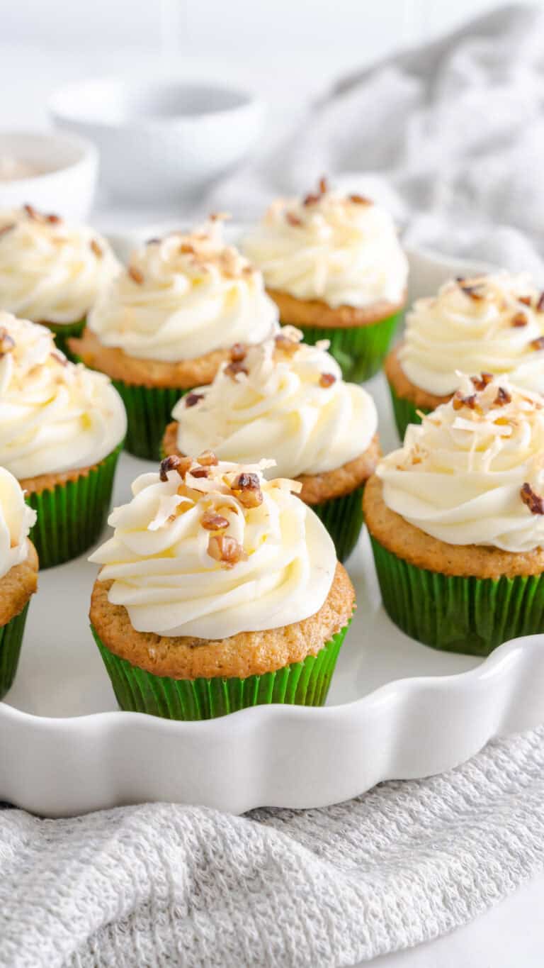 Hummingbird Cake cupcakes in green wrappers and topped with a cream cheese frosting with toasted pecans and coconut.