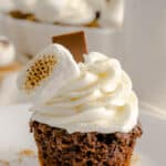 S’Mores chocolate cupcake with a graham cracker crust and white marshmallow frosting on a white plate with crumbled graham cracker crumbs.
