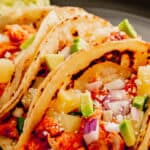 Instant Pot Chicken Al Pastor in corn tortillas topped with cojita cheese, pineapple chunks, and red onion.
