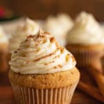 Close up of spice cupcake in white wrapper frosted with cream cheese and decorated with cinnamon.