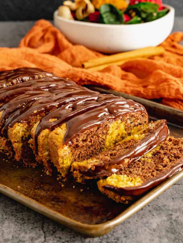Sliced marble cake topped with ganache on dark pan.