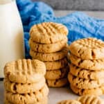 Stacks of brown butter peanut butter cookies with criss cross tops next to a glass jar of milk.