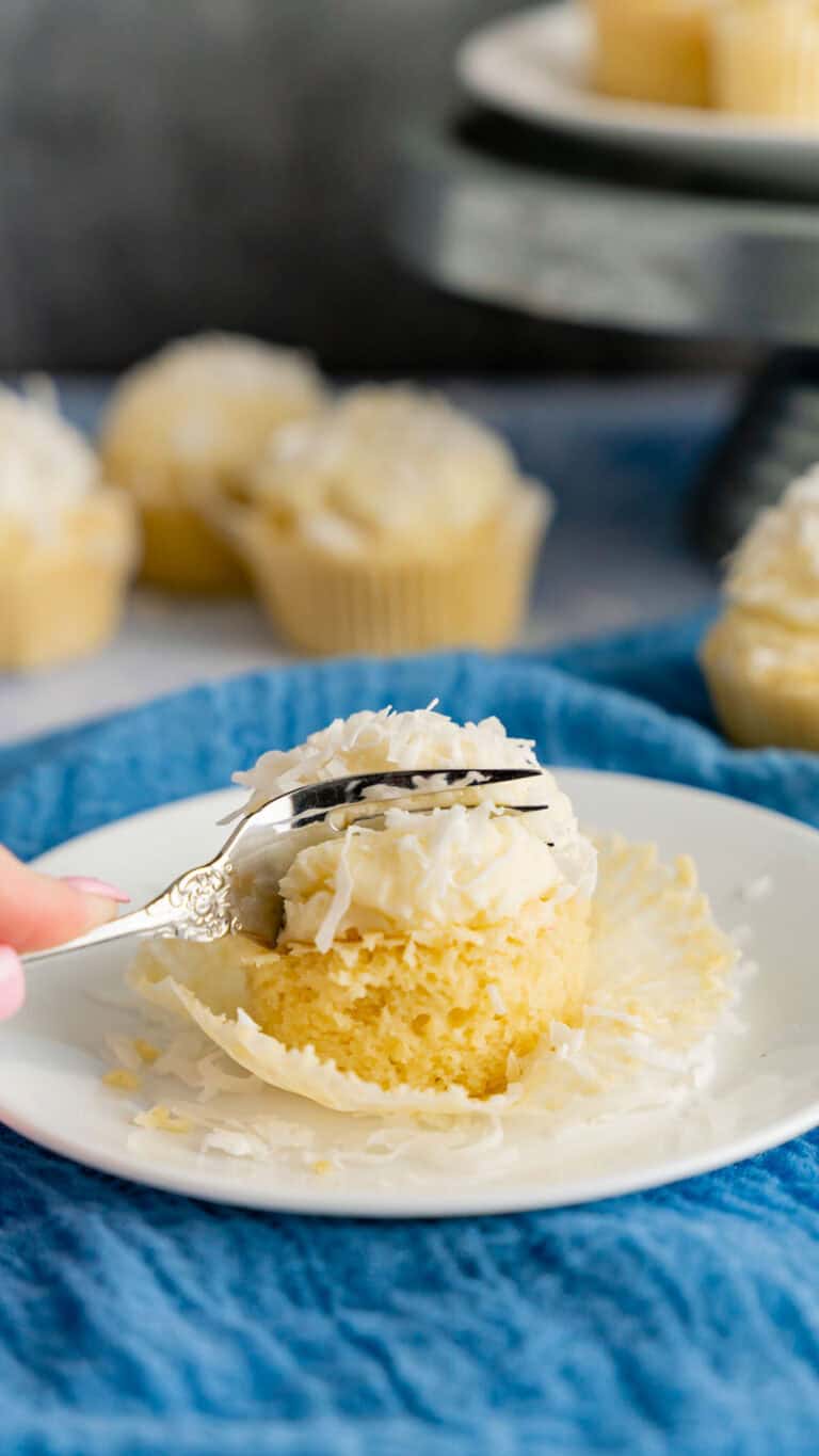 A fork slicing through a coconut cupcake on a blue linen.