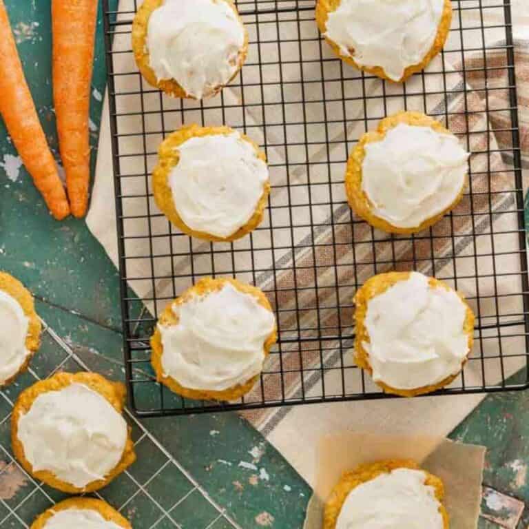 Carrot cookies resting on a wire rack that have been frosted with cream cheese.