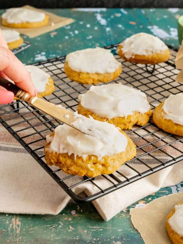 Cream cheese frosting being spread onto a carrot cake cookie.