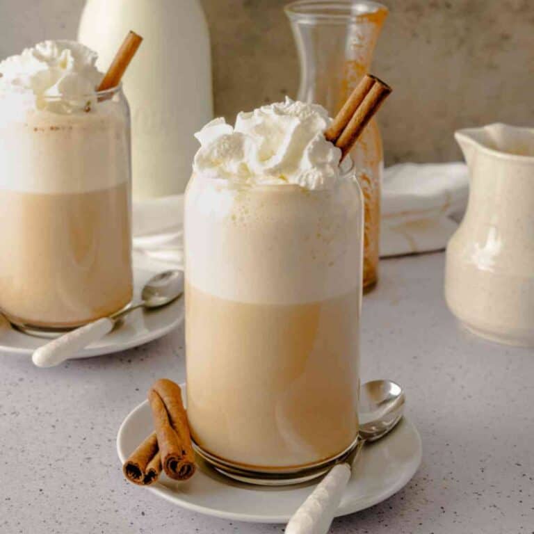 Two glasses of chai tea latte with whipped cream and cinnamon sticks.
