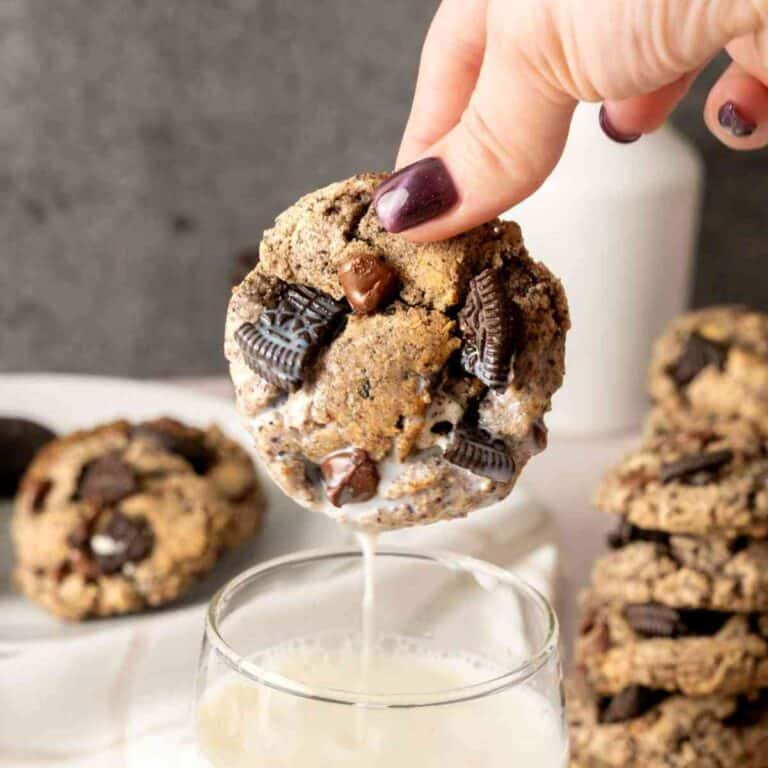 A manicured hand dipping an Oreo Chocolate Chip Cookie into a glass of milk.