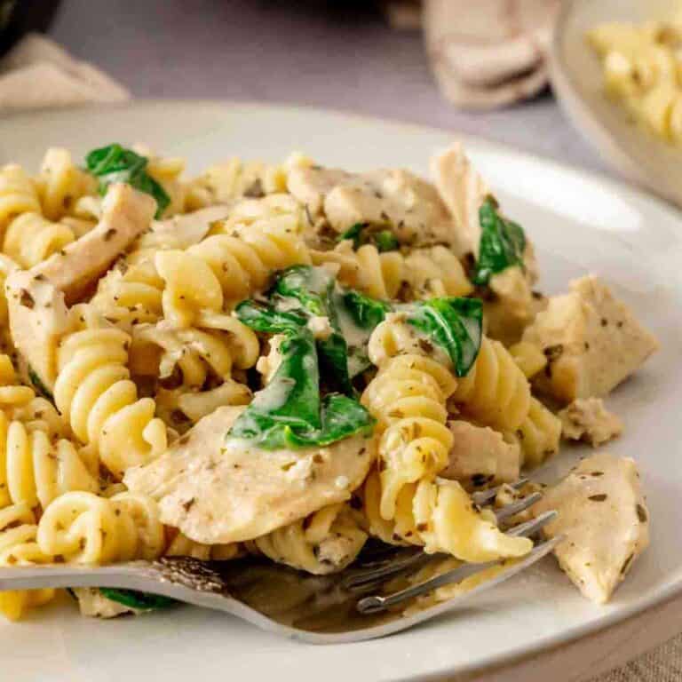 A plate of chicken pesto pasta tossed with spinach that was made in the Instant Pot with a serving of breadsticks in the background.