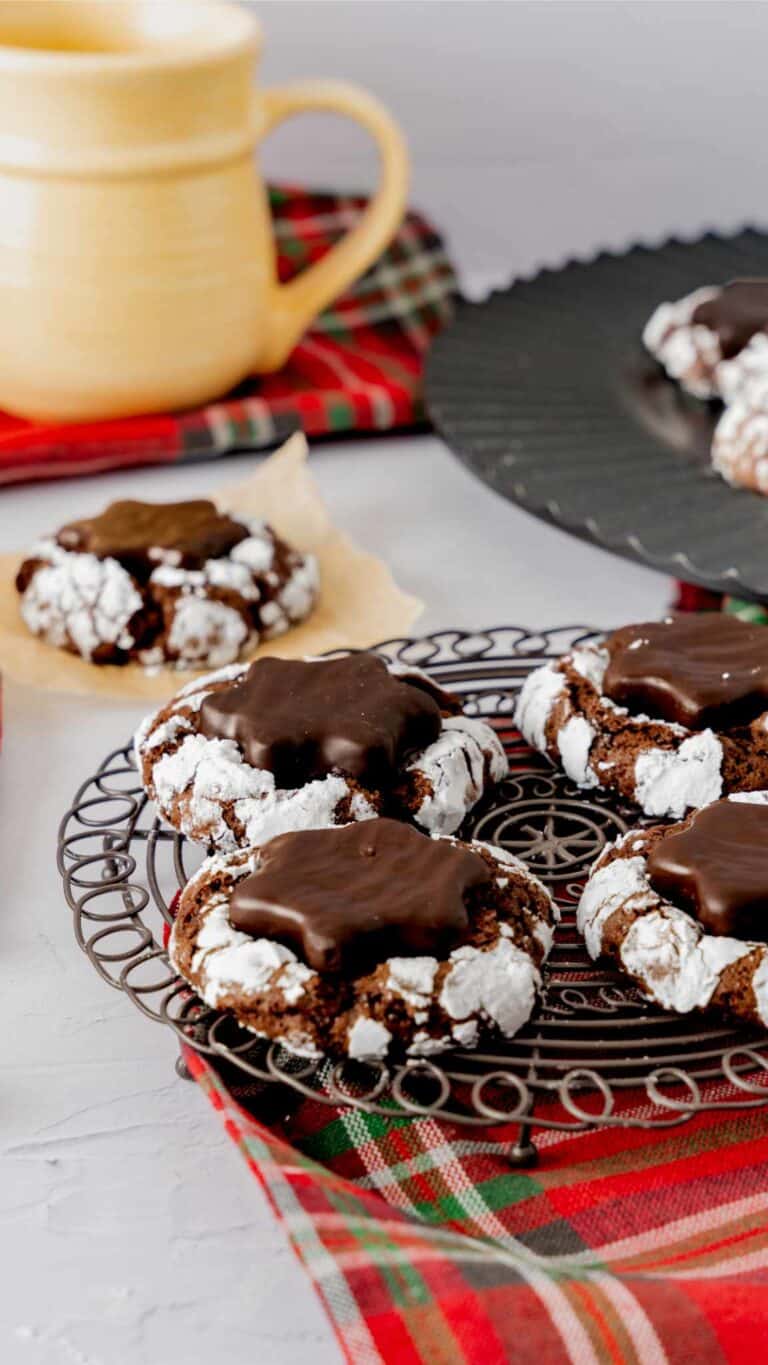 Four hot cocoa crinkle cookies with peppermint patties sitting on a round black cooling rack.