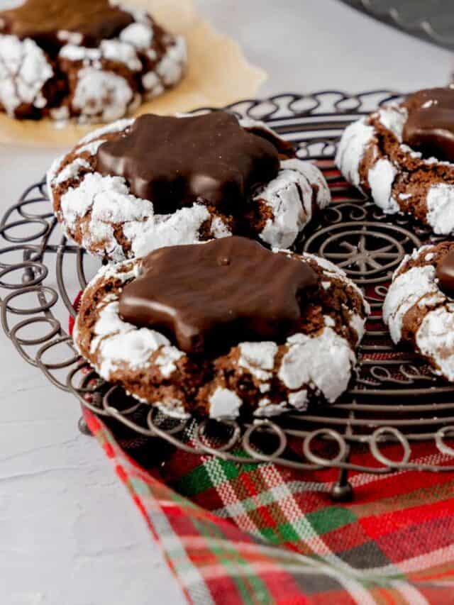 Four hot cocoa crinkle cookies with peppermint patties sitting on a round black cooling rack.