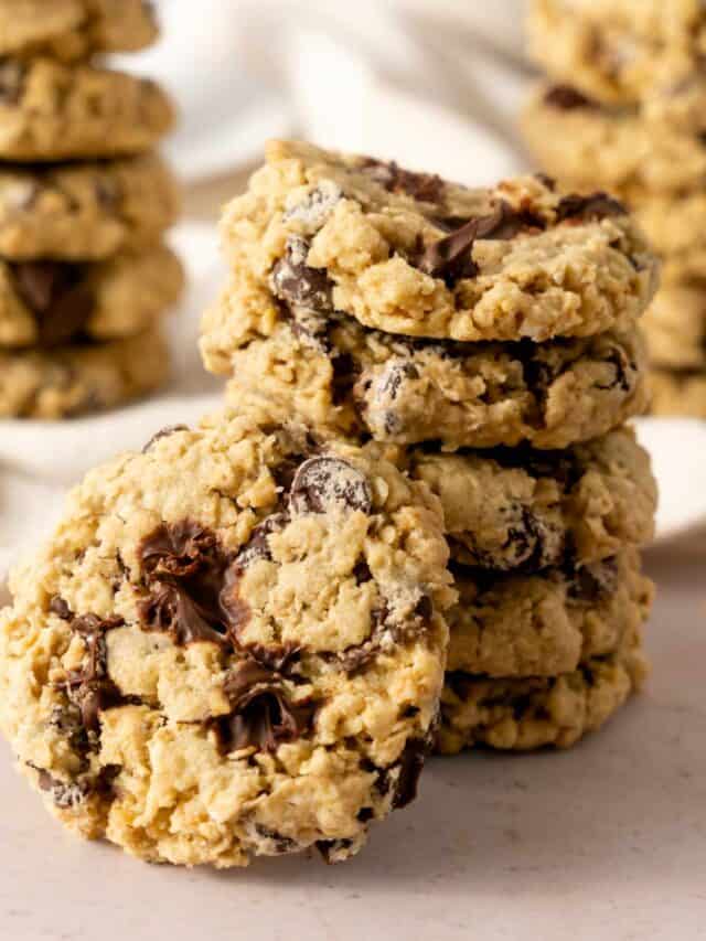 A stack of chocolate chip oatmeal cookies on a beige background with a cookie with melted chocolate.
