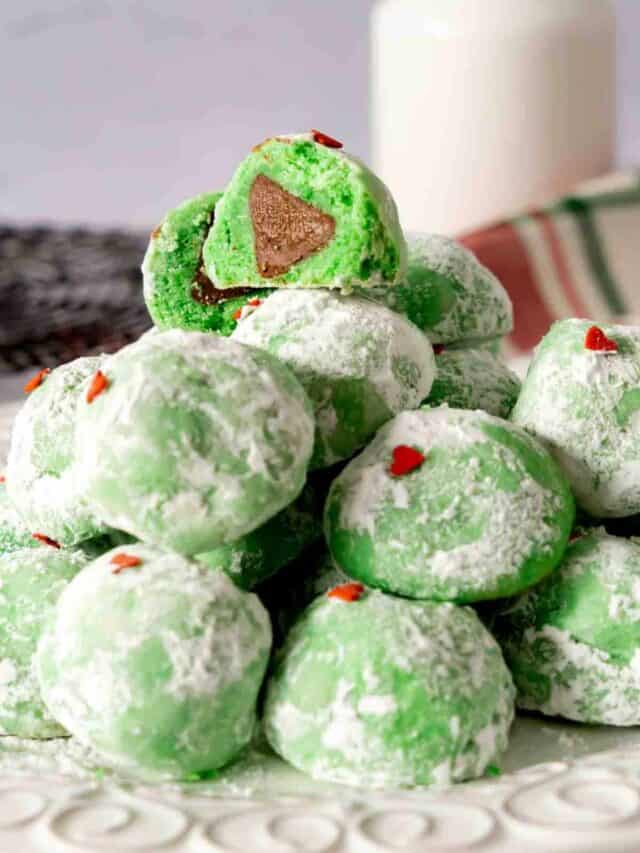 A snowball grinch cookie cut open to see a Hershey kiss baked in the center.