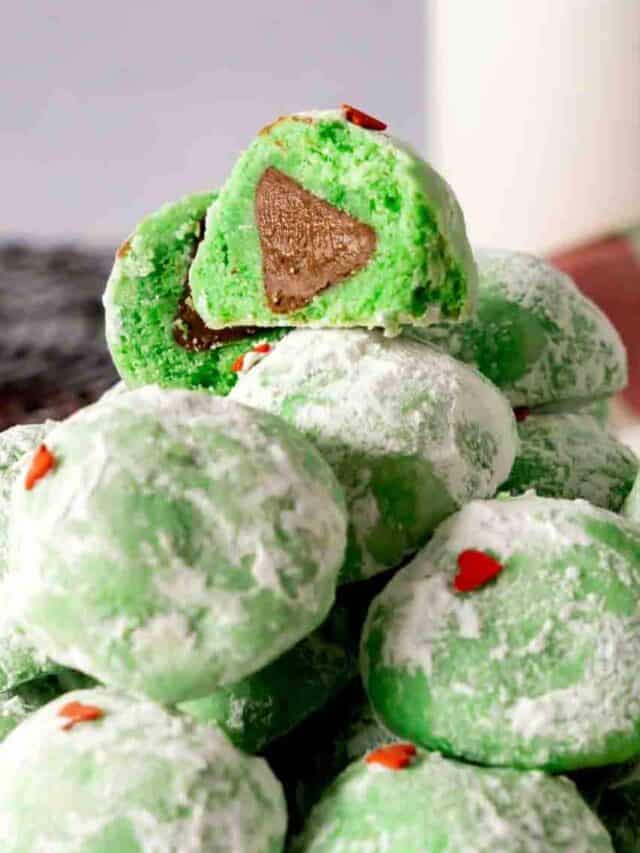 A snowball grinch cookie cut open to see a Hershey kiss baked in the center.