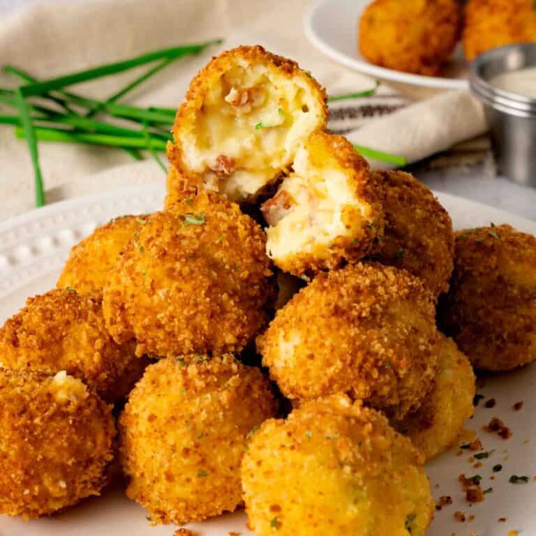 A stack of zesty potato bombs with one cut open to see the melted cheese and mashed potato mixture.