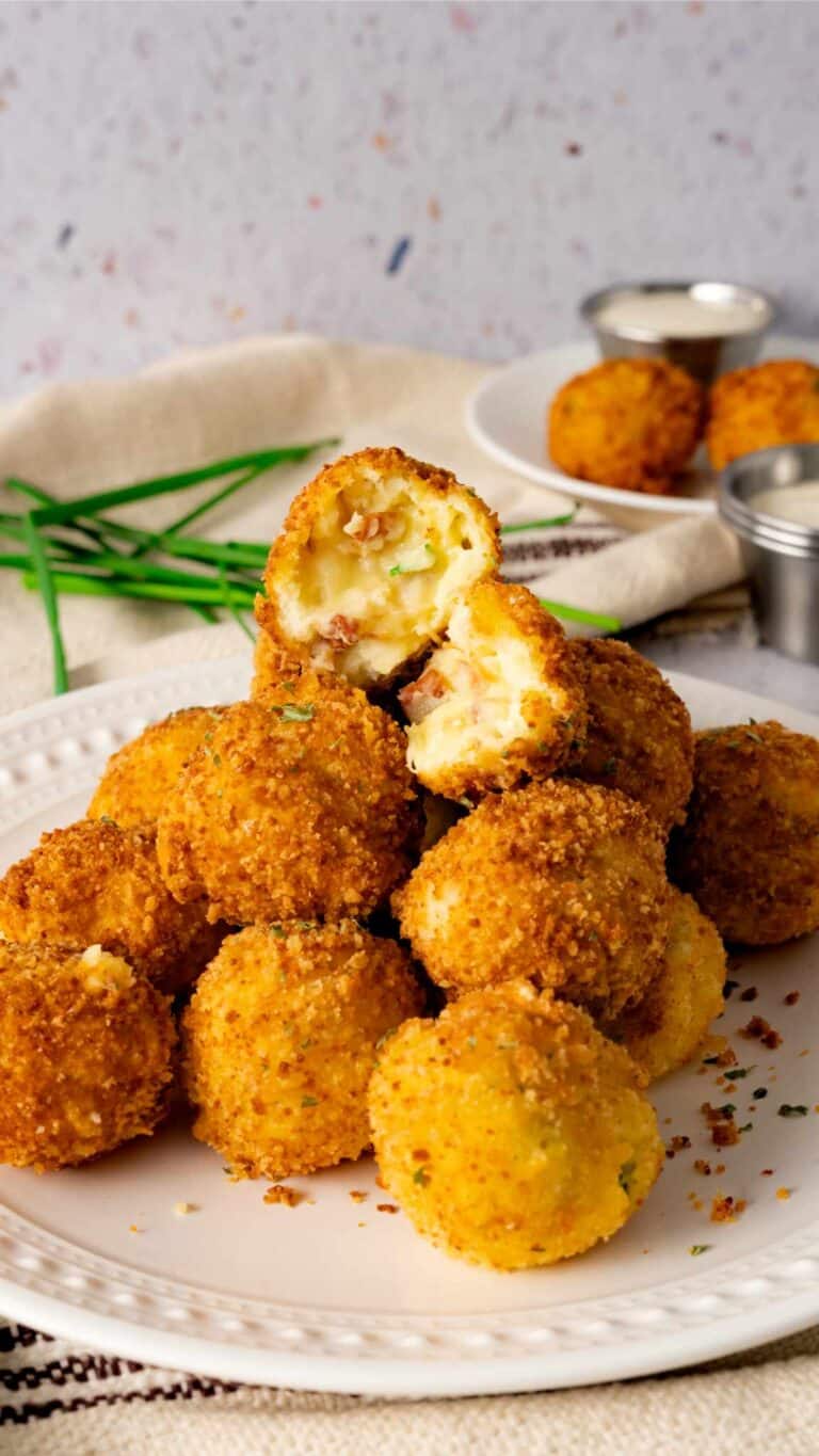 A stack of zesty potato bombs with one cut open to see the melted cheese and mashed potato mixture.
