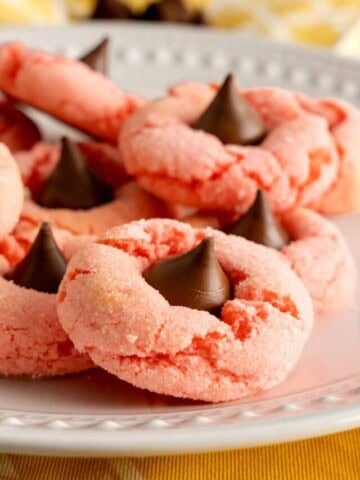 A white plate of strawberry kiss cookies topped with Hershey cookies.