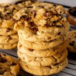 A broken chocolate chip walnut cookie on a stack of cookies.