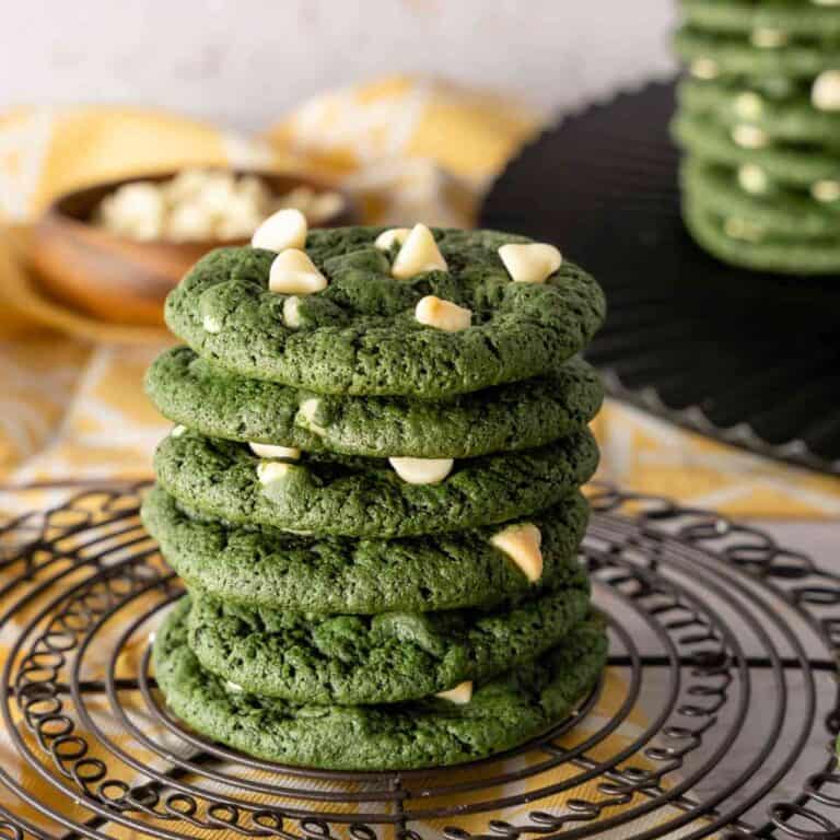 A stack of green velvet cookies with white chocolate chips on a wire round rack with a yellow background.