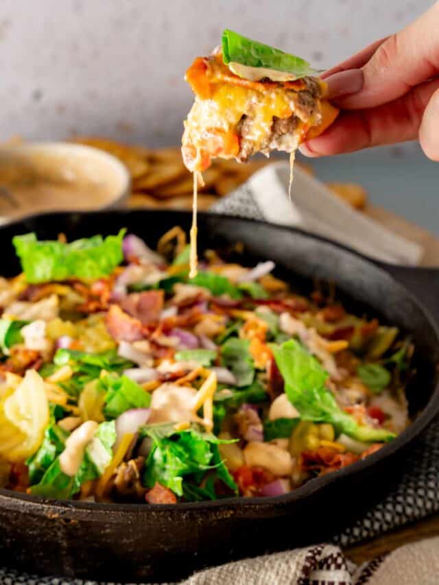 A hand holding up a pretzel of loaded bacon cheeseburger dip.