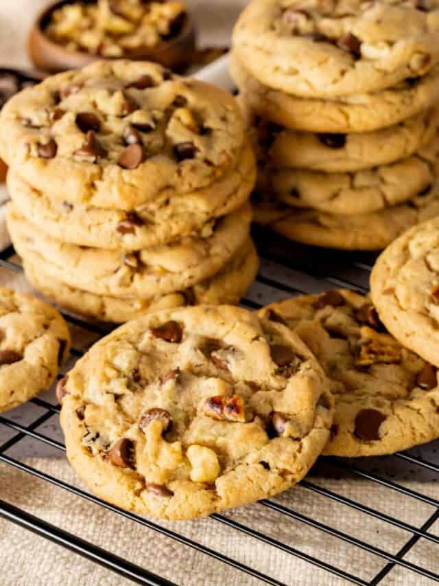 Chocolate chip cookies with toasted walnuts stacked amd spread out on a wire rack.