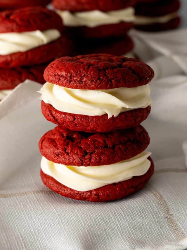 Two Red Velvet Whoopie Pies stacked on top of eachother on a white linen napkin.