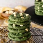 A stack of green velvet cookies with white chocolate chips on a wire round rack with a yellow background.