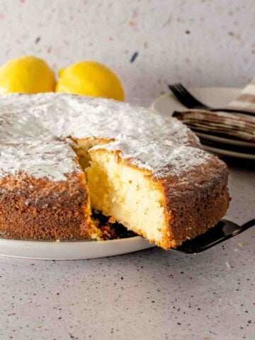 A black cake server pulling a slice of powdered sugar topped lemon and yogurt cake.