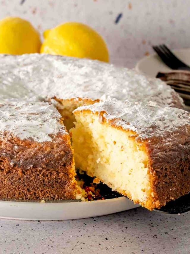 A black cake server pulling a slice of powdered sugar topped lemon and yogurt cake.