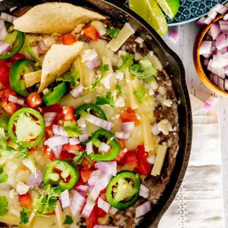 Birdseye view of a cast iron skillet with black bean dip topped with cheese tomatoes, and jalapenos.