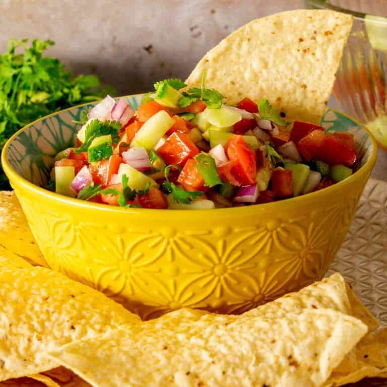 A yellow bowl filled with freshly made cucumber salsa with tortilla chips.