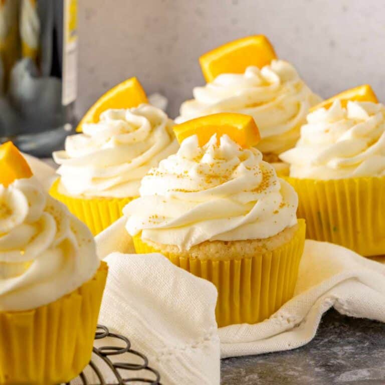 Mimosa cupcakes sitting on white linen with a bottle of prosecco in the background.