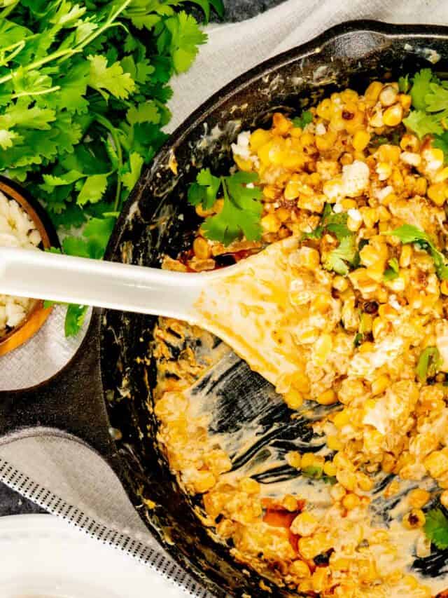 A serving spoon in a cast iron skillet of Mexican street corn dip topped with grilled corn, cheese, and cilantro.