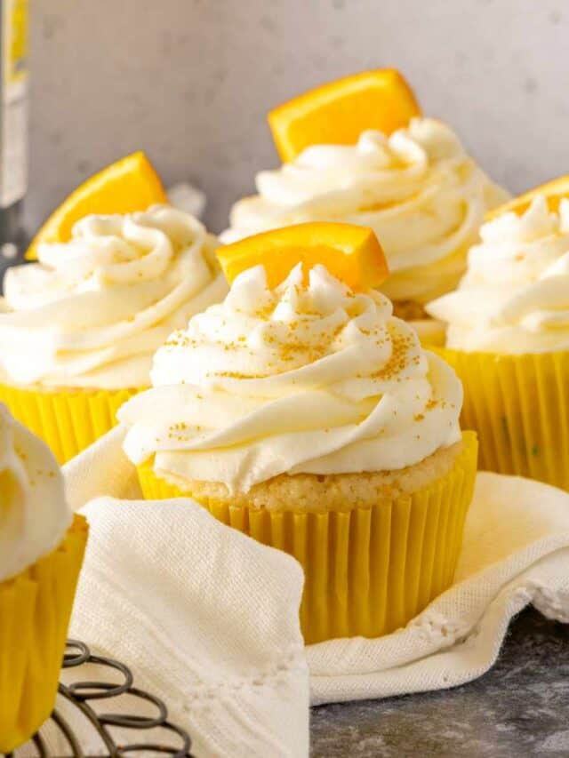 Mimosa cupcakes sitting on white linen with a bottle of prosecco in the background.